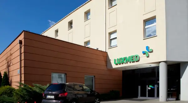 Budynek kliniki Luxmed z zielonym logo, samochód i pomarańczowe pachołki.