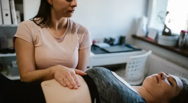 Fizjoterapeutka wykonuje masaż brzucha pacjentce leżącej na kozetce.