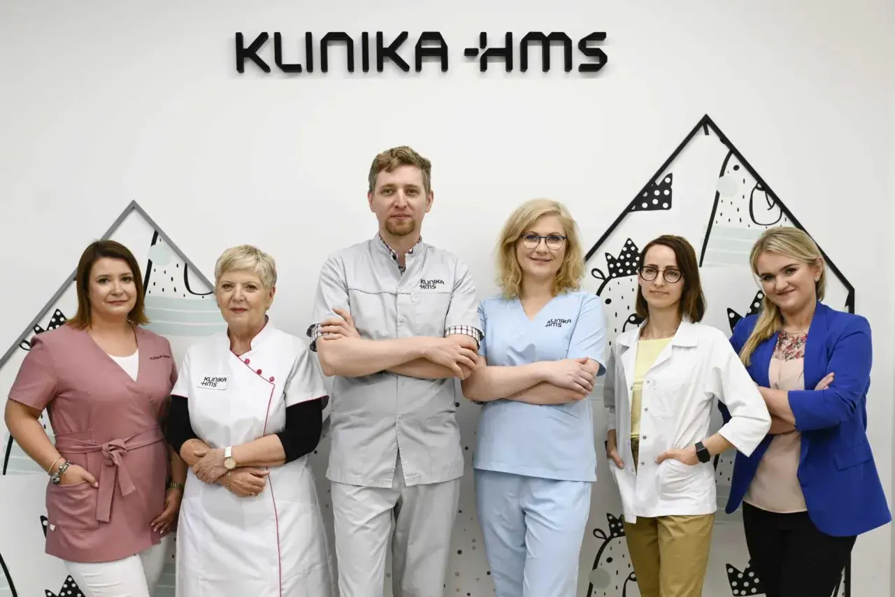 Zespół medyczny w klinice, sześć osób w uniformach medycznych, na tle logo kliniki.