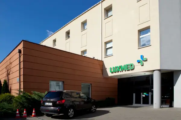 Budynek kliniki Luxmed z zielonym logo, samochód i pomarańczowe pachołki.